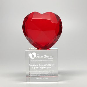 May include: A red crystal heart award on a clear crystal base. The base has the text "the Heart2Heart foundation" and "TheHeart2HeartFoundation.org". The text "Eta Alpha Omega Chapter Alpha Kappa Alpha" is also on the base. The text "Presented in appreciation of your commitment and support as an Outstanding Community Partner" is on the base. The text "February 3, 2018" is on the base.