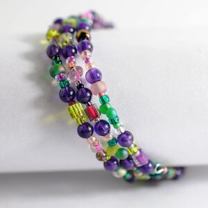 Op de afbeelding: Meerstrengige armband met paarse, groene, roze en transparante kralen. De armband is gemaakt van kralen in verschillende maten en vormen.
