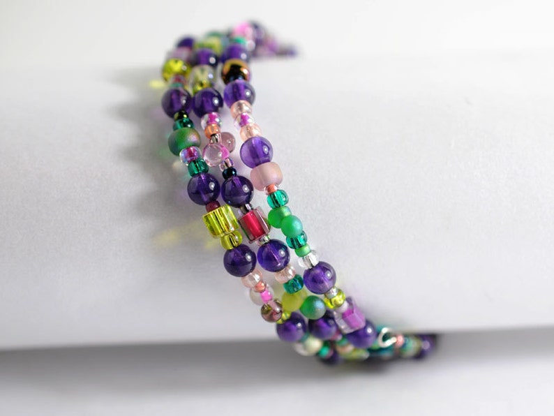 Op de afbeelding: Meerstrengige armband met paarse, groene, roze en transparante kralen. De armband is gemaakt van kralen in verschillende maten en vormen.