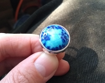 May include: A silver ring with a blue and white cabochon stone set in the center.