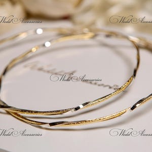 May include: Two gold and silver intertwined bangle bracelets. The bracelets are twisted and have a shiny finish.