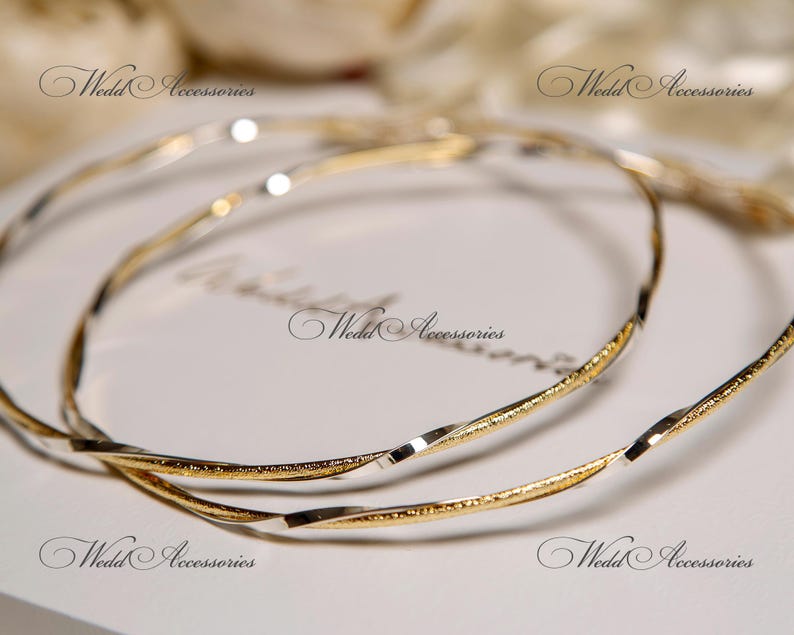 May include: Two gold and silver intertwined bangle bracelets. The bracelets are twisted and have a shiny finish.