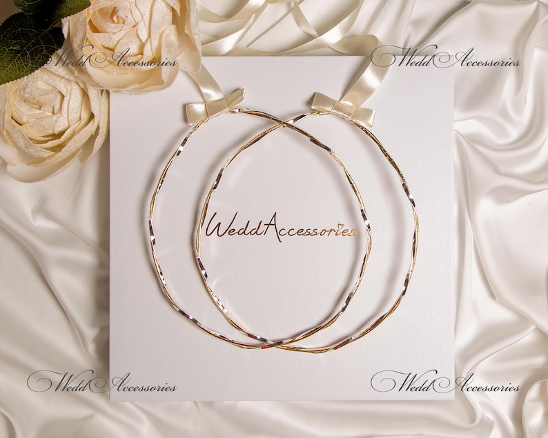 May include: Two gold wedding rings, intertwined, on a white background. The rings are made of a braided metal design.