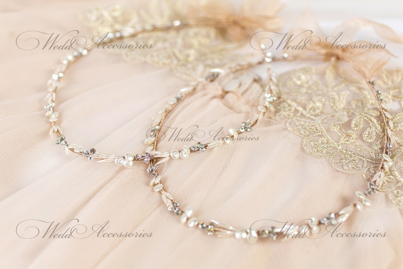 May include: Two delicate bridal headbands with pearl and crystal accents. The headbands are intertwined, resting on a soft, peach-colored fabric. The words "Wedd Accessories" are visible in the image.