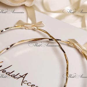 May include: Two gold-toned, twisted metal wedding bands with white satin bows. The bands are on a white background with the text "Wedding Accessories" printed on the surface.