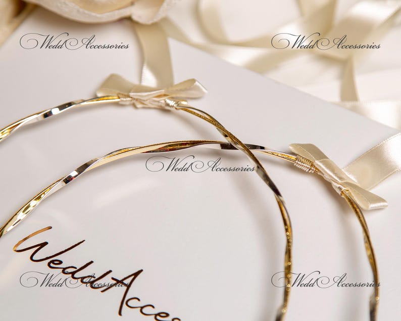 May include: Two gold-toned, twisted metal wedding bands with white satin bows. The bands are on a white background with the text "Wedding Accessories" printed on the surface.