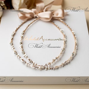 May include: Two bridal headbands with pearl and crystal accents, arranged on a white box with a beige ribbon. The headbands are adorned with delicate floral and crystal details, perfect for a wedding or special occasion. The text "Wedd Accessories" is visible.