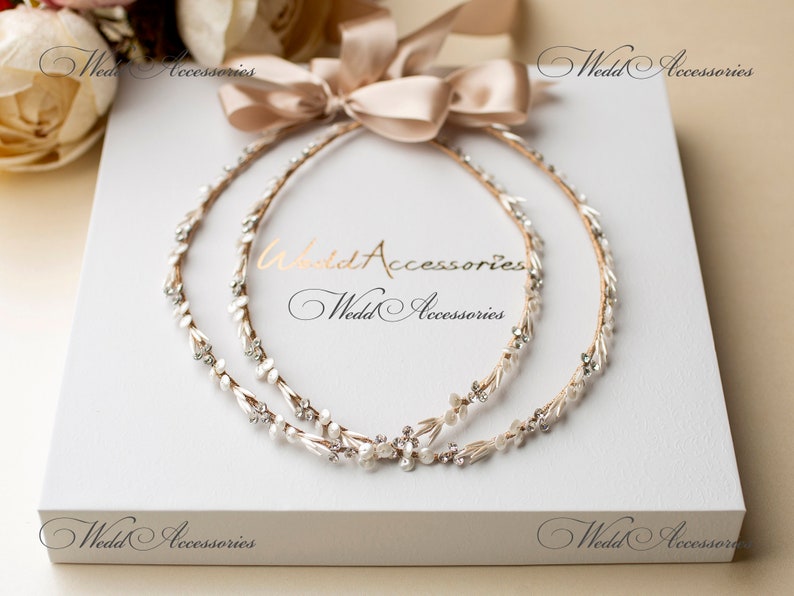 May include: Two bridal headbands with pearl and crystal accents, arranged on a white box with a beige ribbon. The headbands are adorned with delicate floral and crystal details, perfect for a wedding or special occasion. The text "Wedd Accessories" is visible.
