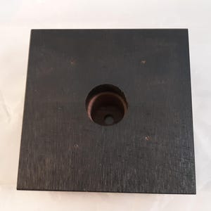 May include: A black square wooden base with a circular hole in the center. The base is made of wood with a dark stain.