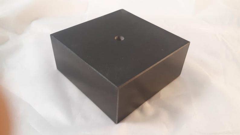 May include: A black square pedestal with a small hole in the center. The pedestal is made of wood and has a smooth finish.