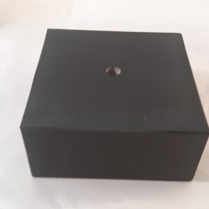 May include: A black square display stand with a small hole in the center.