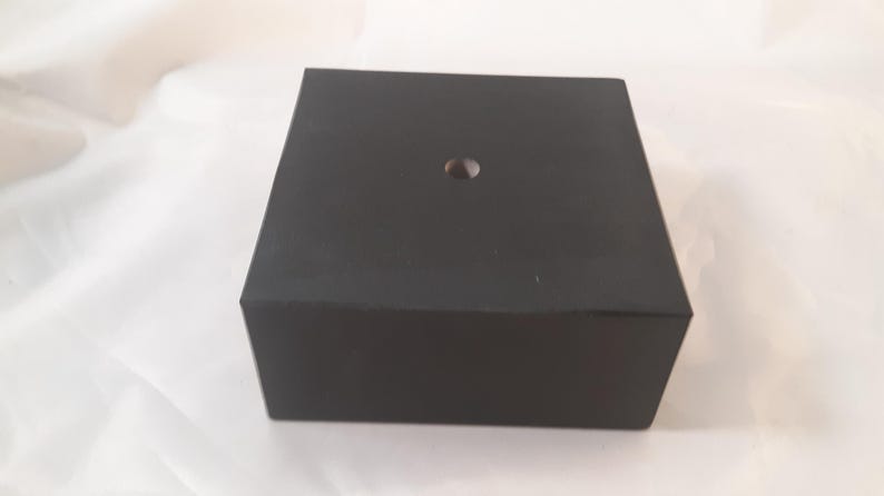 May include: A black square display stand with a small hole in the center.