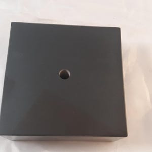 May include: A black square base with a hole in the center. The base is made of a smooth, hard material.