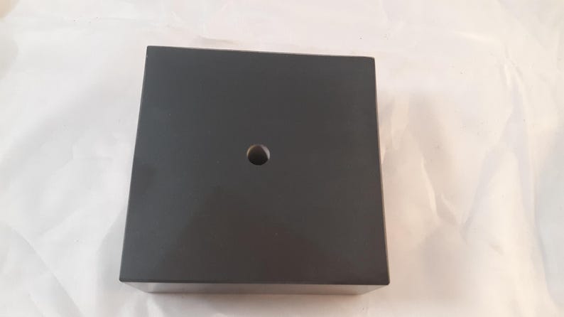 May include: A black square base with a hole in the center. The base is made of a smooth, hard material.