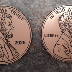 Op de afbeelding: Twee koperkleurige ronde munten met het beeld van Abraham Lincoln. De munten hebben de tekst "IN GOD WE TRUST" en "LIBERTY". E&eacute;n munt is gedateerd 2025, de andere 2000.