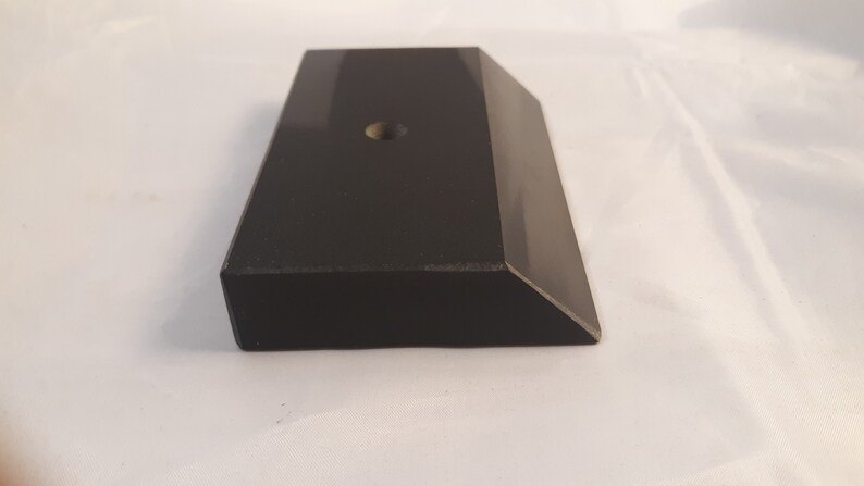 May include: A rectangular black block with a smooth, reflective surface and a beveled edge on one side. The top surface features a single, centered circular hole. The object has a solid, uniform dark appearance with sharp, clean geometric lines.