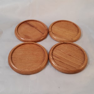 May include: Four round wooden coasters with a natural wood finish. The coasters are smooth and have a slightly raised edge.