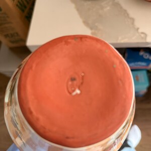 May include: A ceramic bowl with a peach-colored interior and a checkered pattern in peach and white on the exterior. The bowl's base is a solid peach color, and the rim has a floral design.