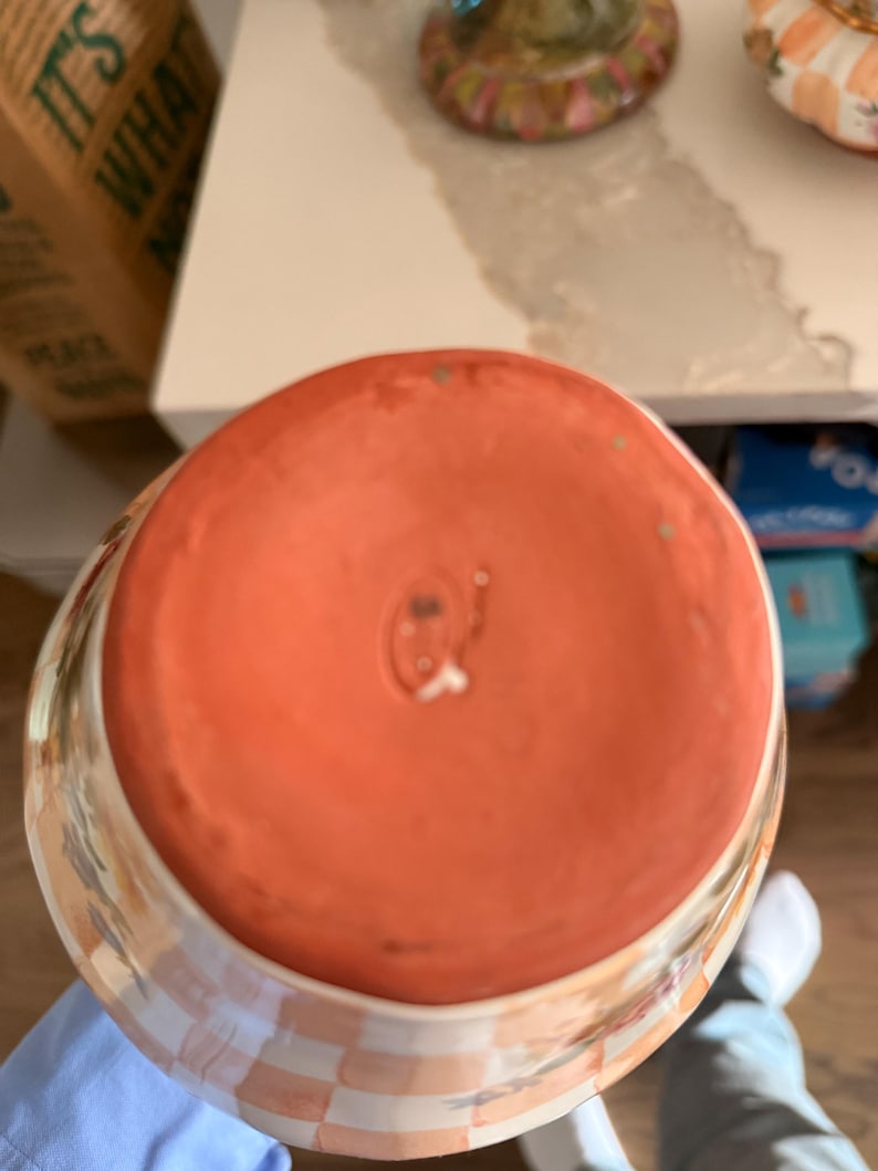 May include: A ceramic bowl with a peach-colored interior and a checkered pattern in peach and white on the exterior. The bowl's base is a solid peach color, and the rim has a floral design.