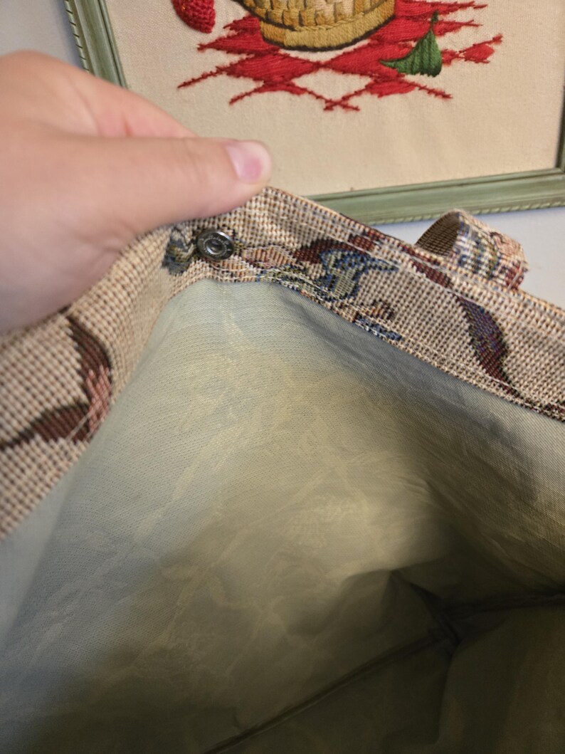 May include: A vintage tapestry tote bag with a floral pattern in shades of brown, blue, and red. The interior is a light green fabric. The bag has a snap closure and a handle.