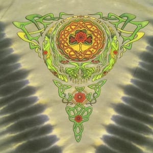 Puede incluir: Camiseta te&ntilde;ida con un dise&ntilde;o detallado de nudo celta en verde, amarillo y rojo. El motivo central presenta una calavera estilizada y elementos florales, sobre un fondo gris y beige arremolinado.