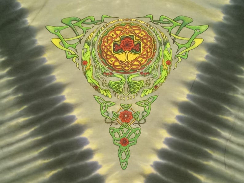 Puede incluir: Camiseta te&ntilde;ida con un dise&ntilde;o detallado de nudo celta en verde, amarillo y rojo. El motivo central presenta una calavera estilizada y elementos florales, sobre un fondo gris y beige arremolinado.