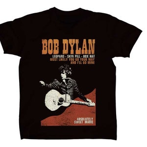 May include: Black t-shirt with a vintage-style graphic of Bob Dylan playing a guitar. The text reads "BOB DYLAN, LEOPARD-SKIN PILL-BOX HAT, MOST LIKELY YOU GO YOUR WAY AND I'LL GO MINE, ABSOLUTELY SWEET MARIE."