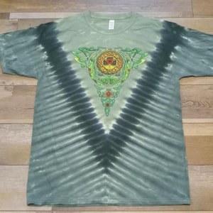 Puede incluir: Camiseta te&ntilde;ida con tinte anudado en tonos verdes y negros, con un dise&ntilde;o central de nudo celta en verde, amarillo y rojo. La camiseta tiene cuello redondo y mangas cortas, con un patr&oacute;n de rayas verticales.