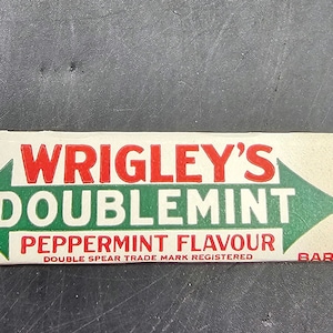 May include: A white, rectangular package of Wrigley's Doublemint Peppermint Flavour chewing gum. The package has red and green text and a green arrow pointing to the right.