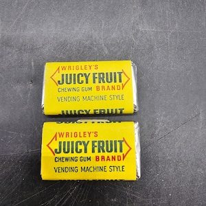 May include: Two yellow and red wrappers for Wrigley's Juicy Fruit chewing gum. The wrappers have the text "Wrigley's Juicy Fruit Chewing Gum Brandy Vending Machine Style" printed on them.