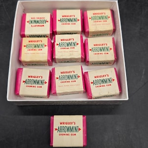 May include: A box of vintage Wrigley's Arrowmint chewing gum. The box contains 10 packs of gum, each with a red and white wrapper featuring the brand name and logo. The gum is a classic flavor and is a popular choice for collectors.