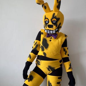 May include: A yellow rabbit costume featuring black distressed markings, a purple bow tie, and a large headpiece with one bent ear. The outfit includes a yellow vest, arm guards, and leg guards worn over a black base layer with black gloves.