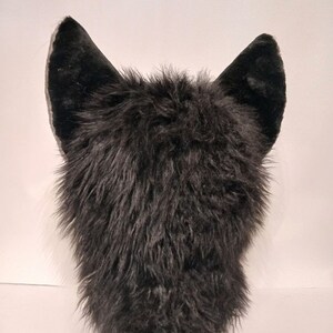 May include: Black furry wolf head with large, black ears. The fur is soft and fluffy.