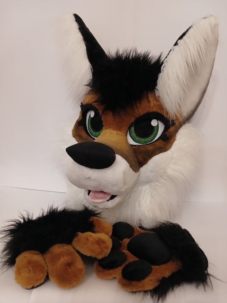 May include: A plush wolf head with black and white fur, brown and black paws, and green eyes. The wolf is smiling with its tongue sticking out.