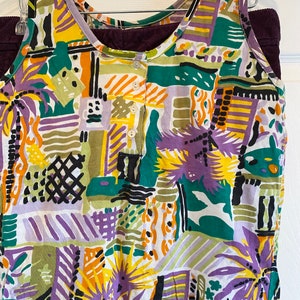 May include: A sleeveless top with a white background and a colorful abstract pattern in shades of purple, yellow, green, and orange. The top has a button closure at the neckline.