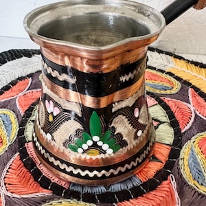 May include: A white ceramic mug with a black handle and the text "But First, Coffee" in a black, bold font. The mug is sitting on a wooden surface. The mug is approximately 4 inches tall.