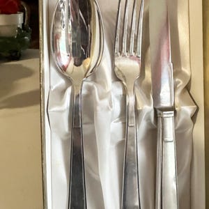 以下が含まれることがあります： 白いサテン張りの箱に入った、スプーン、フォーク、ナイフの3点セットの銀メッキベビーカトラリーです。