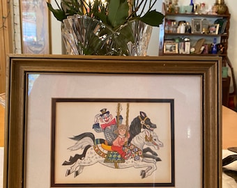May include: A framed illustration of a clown and a child riding a carousel horse. The clown is wearing a red and white costume and a black hat. The child is wearing a red and white dress. The horse is white with black markings.