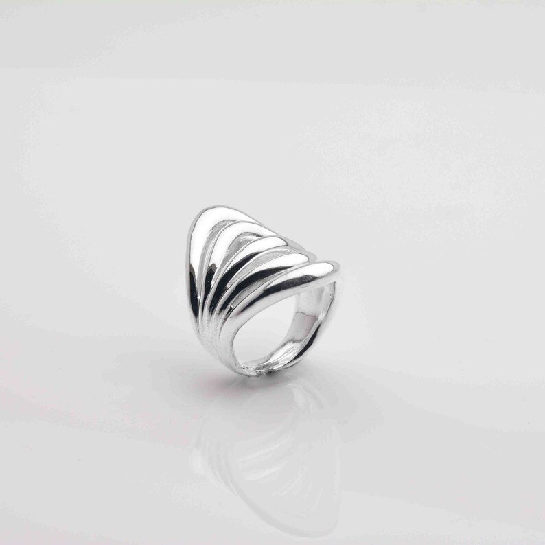 May include: A silver ring with a unique design featuring multiple overlapping curved bands.