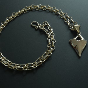 May include: A silver chain necklace with a silver pendant shaped like a sharp, geometric heart.
