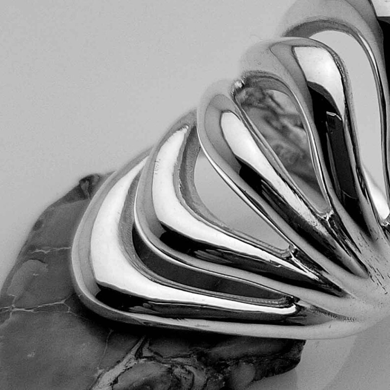 May include: A silver ring with a unique, abstract design. The ring features multiple curved, overlapping bands that create a flowing, organic shape.