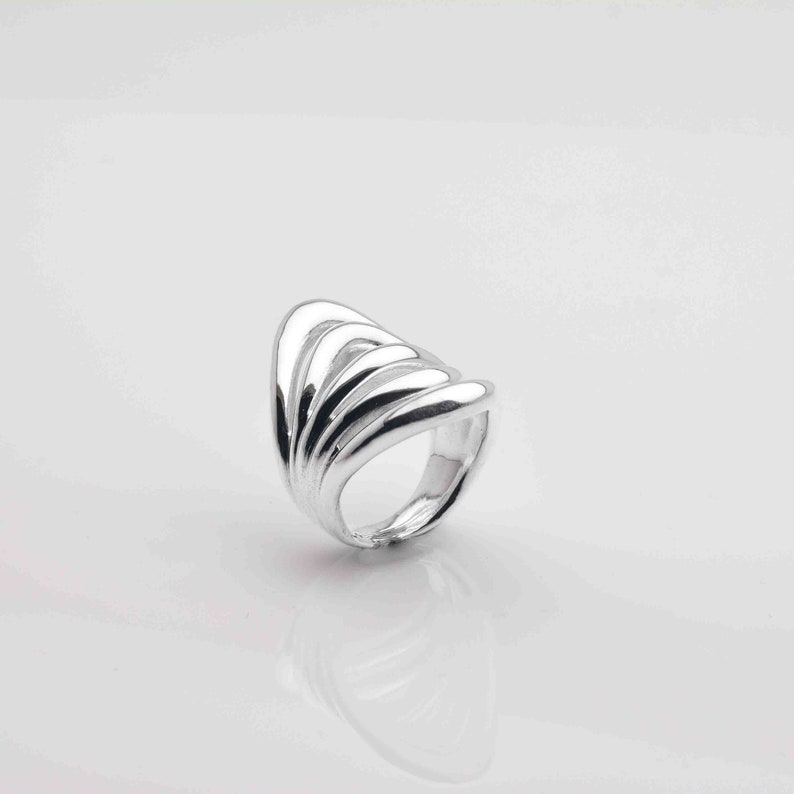 May include: A silver ring with a unique design featuring multiple curved bands that create a wave-like effect.