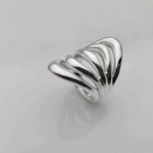 May include: A silver ring with a unique, abstract design. The ring is made of multiple, overlapping bands that create a flowing, organic shape.