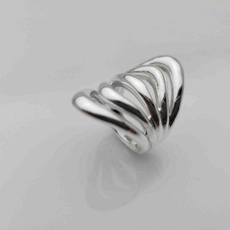 May include: A silver ring with a unique, abstract design. The ring is made of multiple, overlapping bands that create a flowing, organic shape.