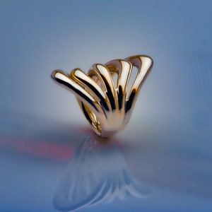May include: A gold ring with a unique, abstract design. The ring is made of multiple curved, interwoven bands that create a flowing, organic shape.