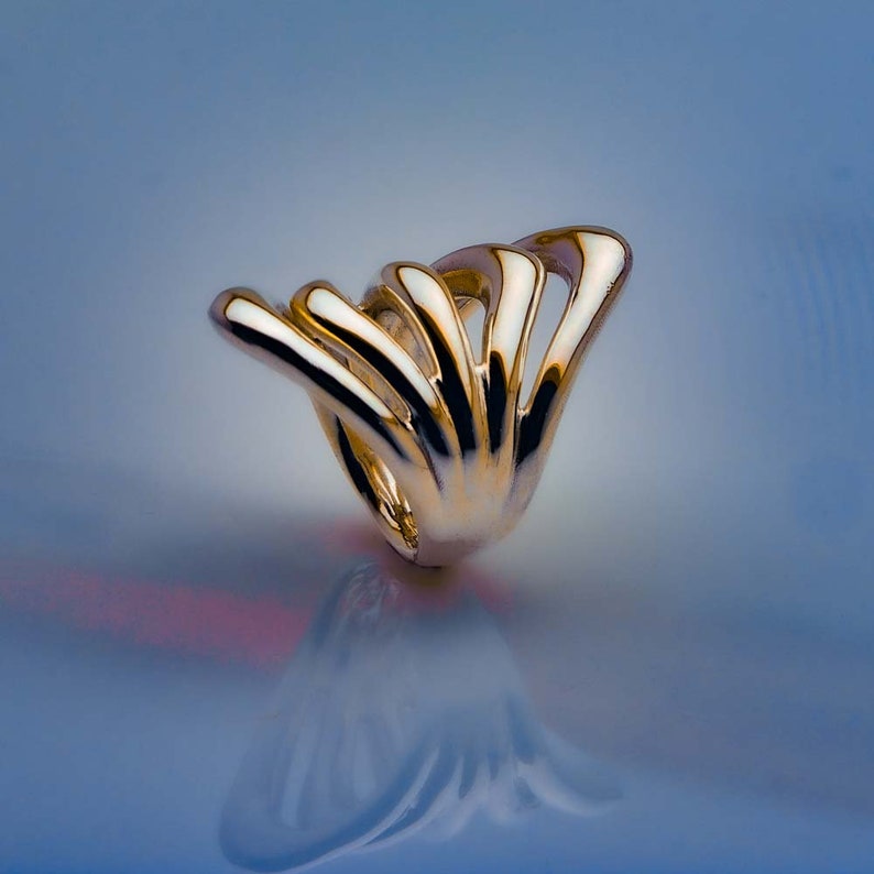 May include: A gold ring with a unique, abstract design. The ring is made of multiple curved, interwoven bands that create a flowing, organic shape.