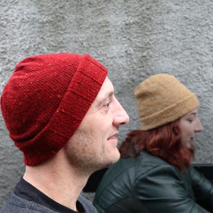 May include: Two people wearing beanies. The person on the left is wearing a red beanie with a textured surface. The person on the right is wearing a yellow beanie.