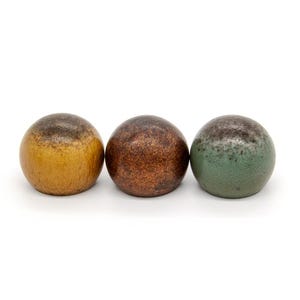 Pode incluir: Três esferas de cerâmica, uma amarela, uma marrom e uma verde, com um esmalte salpicado.