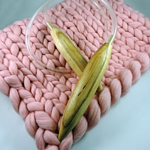 May include: A pair of wooden knitting needles with clear plastic tubing, resting on a pink knitted blanket.