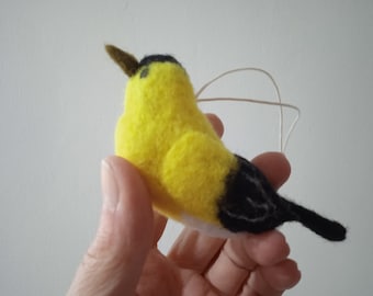 May include: A yellow and black felt bird ornament with a white belly. The bird has a small brown beak and is hanging from a white string.